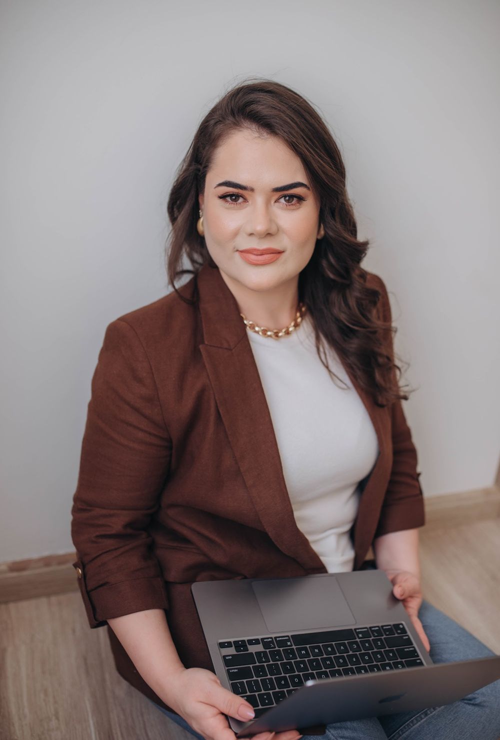 Dra. Karine Homem sorrindo, de blazer marrom, com o notebook