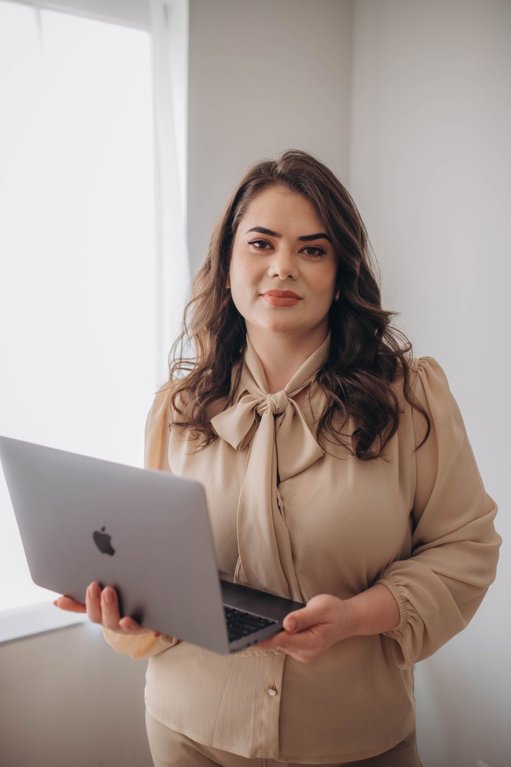 Dra. Karine Homem em pé, de blazer branco e blusa bege, segurando o notebook